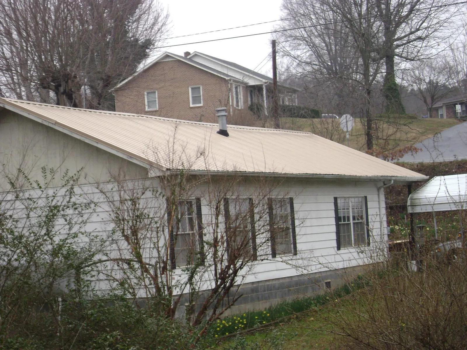 Tan metal roof on a white sided house set into a hillside — Commercial Roofing by Roofing Brothers in Athol
